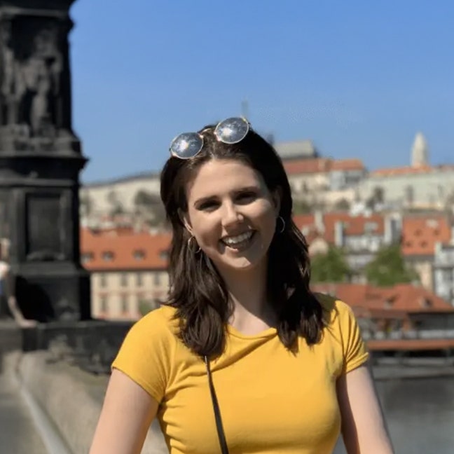 Amelia smiles with sunglasses on her head in front of an urban background
